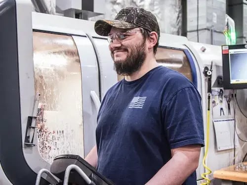 Machine operator wearing safety glasses monitors a CNC machining process.